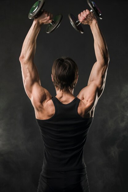 Back view of muscled man lifting up weights