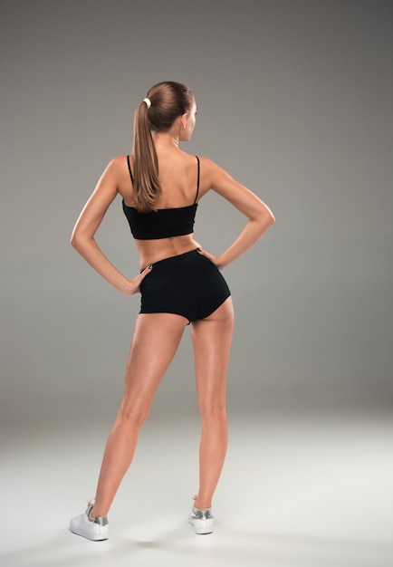 The back view of muscular young woman athlete posing on gray