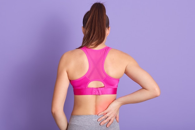無料写真 スタジオで紫色の壁に立っている背中の痛みを持つ若い女性の背面図