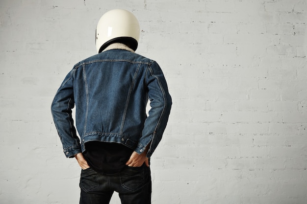 無料写真 younfモトサイクリストのフィットボディの背面図は、ズボンの後ろポケットに手を入れて、ヘルメット、黒の長袖ヘンリーシャツ、クラブデニムジャケットを着ています。
