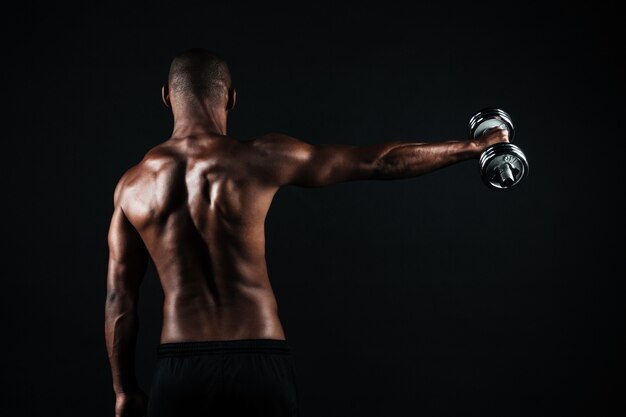 Back view photo of half-naked muscular sports man, with dumbbell in right hand