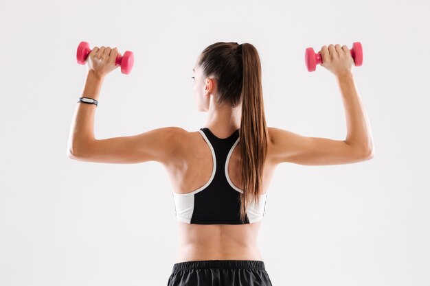 Back view portrait of a healthy slim sportswoman holding dumbbells