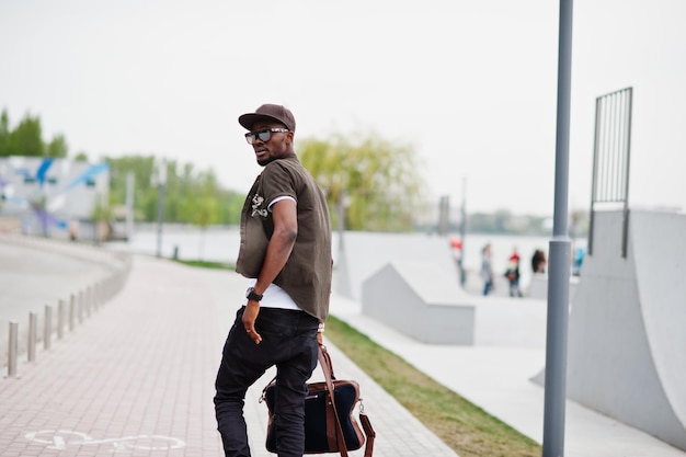 Вид сзади портрет ходячего стильного афроамериканца в солнцезащитных очках и кепке с сумочкой на улице Уличная мода темнокожий мужчина