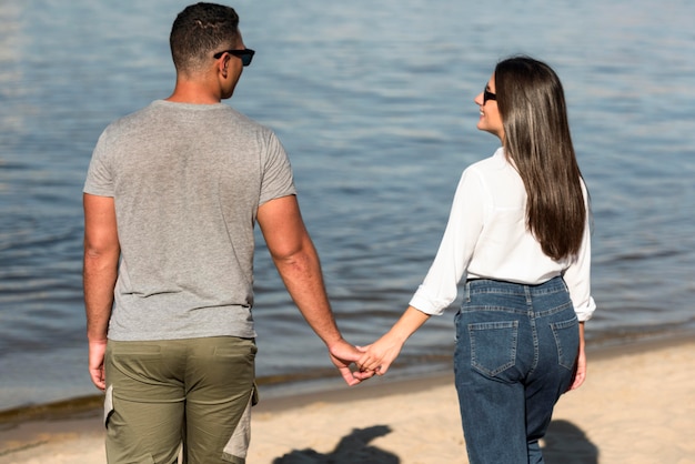 Back view of romantic couple holding hands on the beach