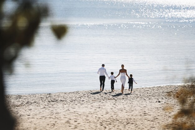 Вид бегущей семьи на пляже в солнечный день у моря в модной одежде