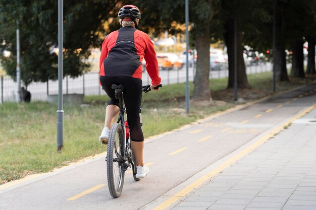 Back view of senior woman riding bike outdoors with copy space