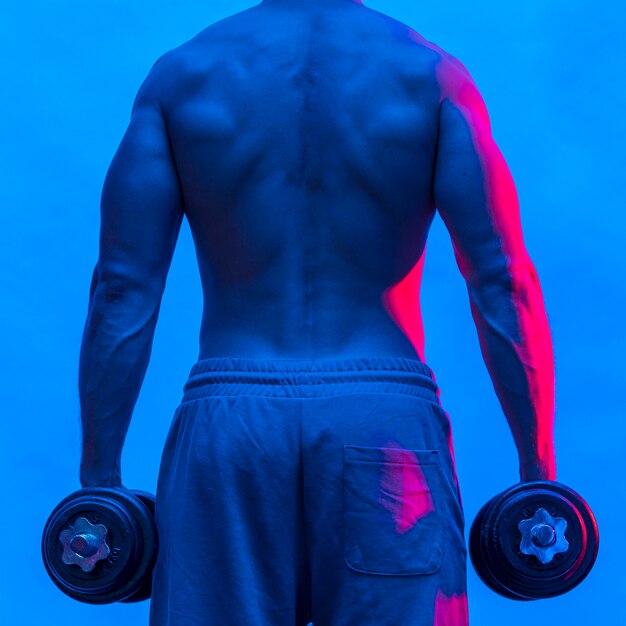 Back view of shirtless fit man holding weights