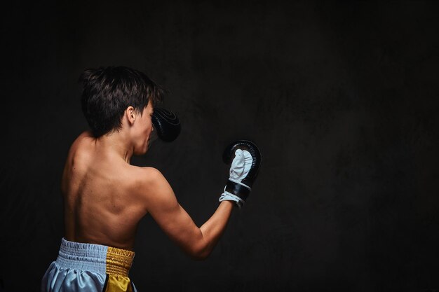 Вид сзади молодого боксера без рубашки во время боксерских упражнений, сосредоточенный на процессе с серьезным сосредоточенным лицом.