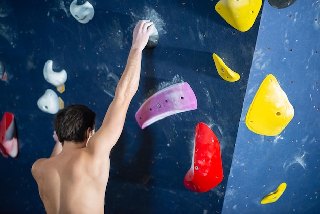 Free photo back view of slim man training. sportsman in dark clothes at bouldering wall. sport, hobby, wellbeing concept