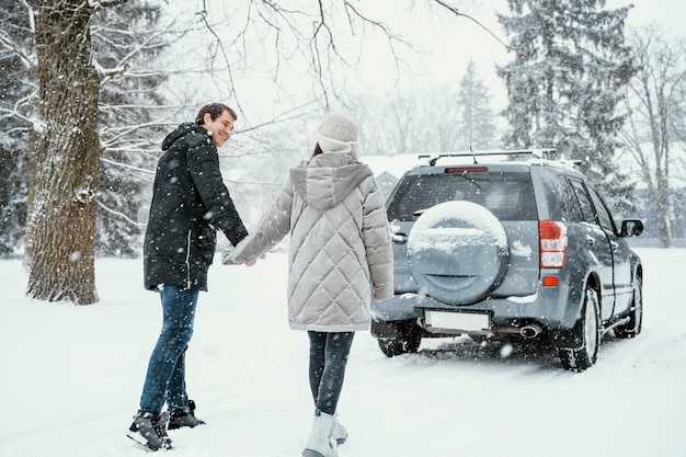Back view of smiley couple enjoying the snow while on a road trip