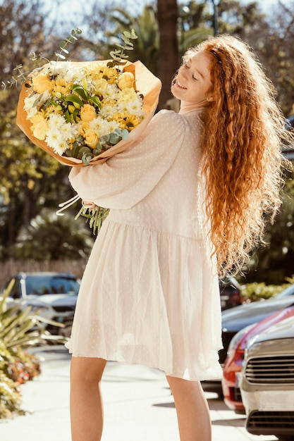 春の花の花束と屋外の笑顔の女性の背面図