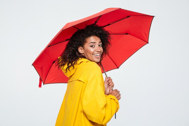 傘の下に隠れているレインコートで笑顔の女性の背面図