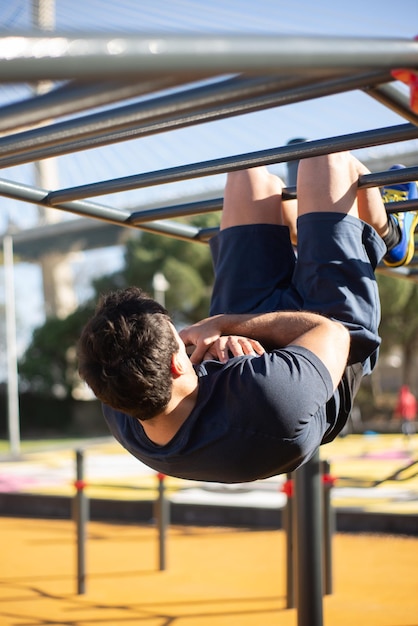 Вид сзади на спортсмена, работающего в солнечный день. Мужчина в спортивной одежде на открытой спортивной площадке, приседает вверх ногами на брусьях. Спорт, здоровье, концепция разработки