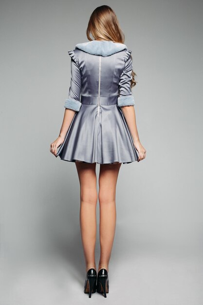 Back view of tall model wearing pretty grey dress decorated with fur on collar and sleeves Wearing black high heels Isolate