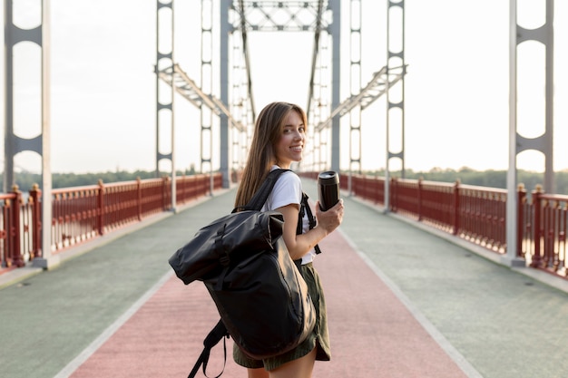 Back view of traveling woman with backpack holding thermos while traveling