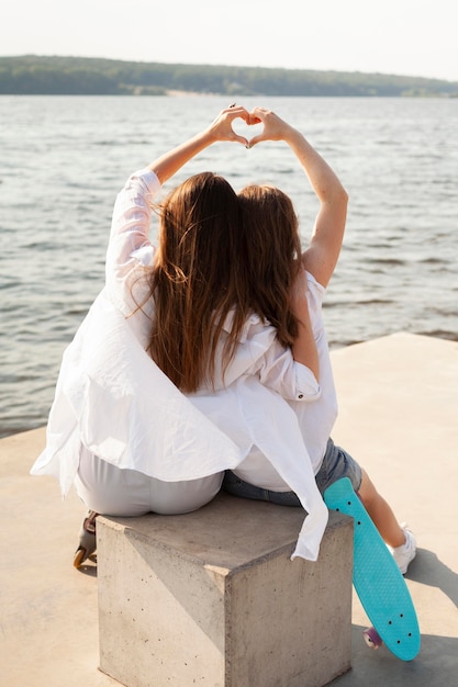 Vista posteriore di due donne che fanno il segno di amore in riva al lago