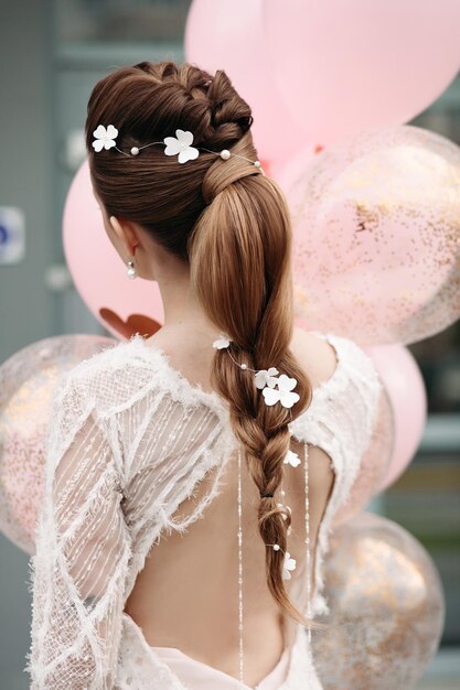 분홍색 공기 풍선에 무리가 있는 고급스러운 흰색 드레스를 입고 포즈를 취한 아름다운 머리와 꽃을 가진 알아볼 수 없는 화려한 브루네트의 뒷모습