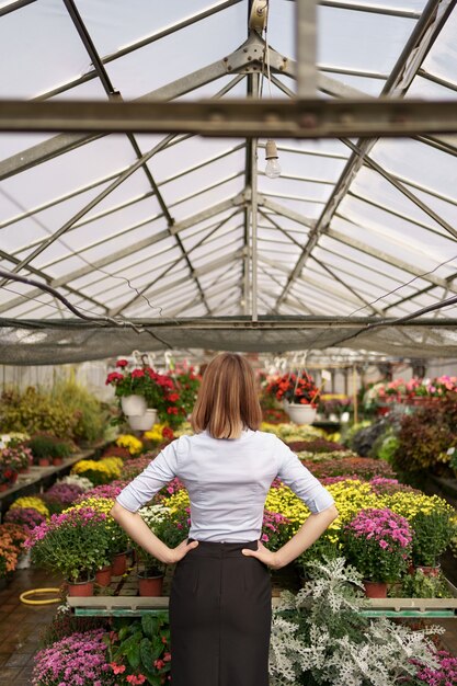 彼女の仕事の結果を見ている女性起業家の背面図。さまざまな種類の花を見ている温室の所有者