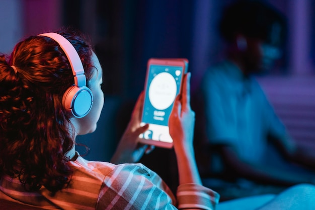 Free photo back view of woman at home using headphones and tablet