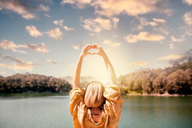 Back view woman making heart-shaped hands on a sunset