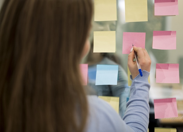 Free photo back view of woman in office writing on sticky notes