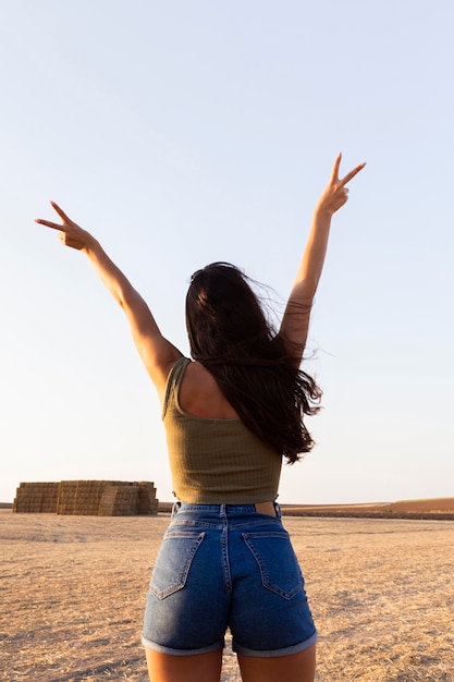 Foto gratuita vista posteriore della donna all'aperto facendo segno di pace con entrambe le mani