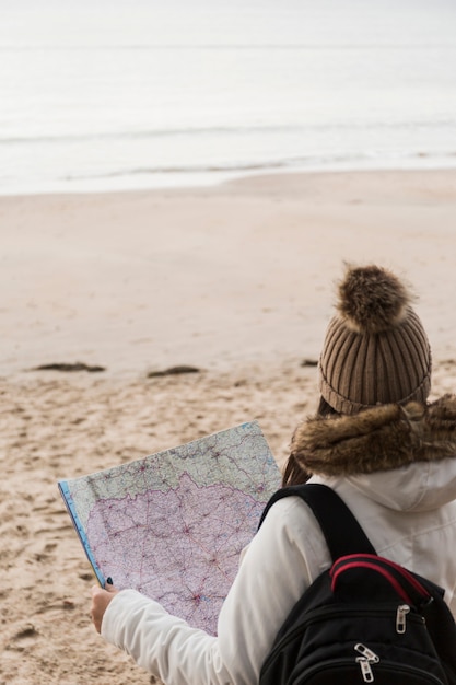 Free photo back view woman reading map on seashore