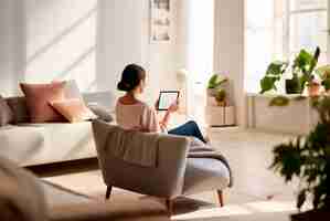 Free photo back view of woman sitting on couch with tablet