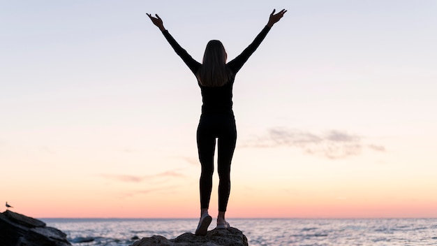 Back view woman standing on a coast with her arms up