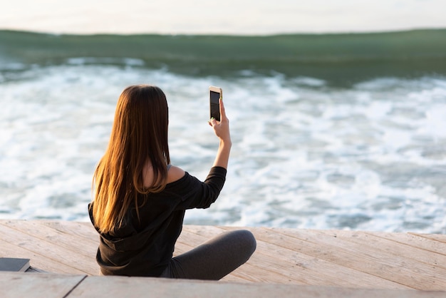 Foto gratuita donna di vista posteriore che cattura una foto del mare