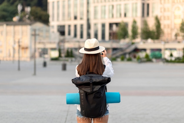 Back view of woman taking pictures while traveling with back pack