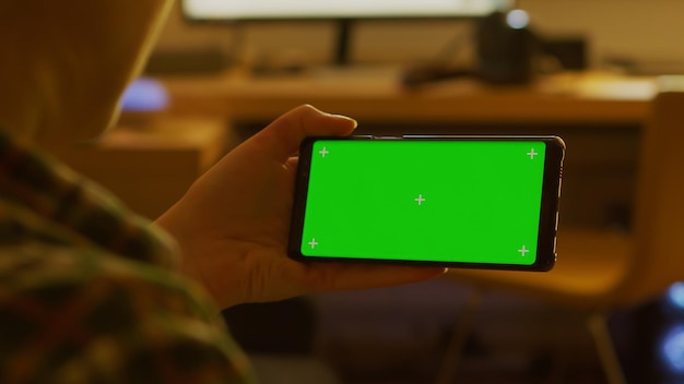 Вид сзади женщины, использующей смартфон с макетом зеленого экрана
