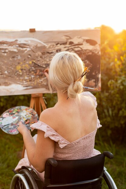 Вид сзади женщины в инвалидной коляске, живопись на открытом воздухе