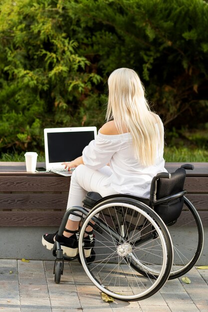 Back view of woman in wheelchair using laptop outdoors