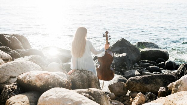Вид сзади женщины с виолончелью на берегу океана