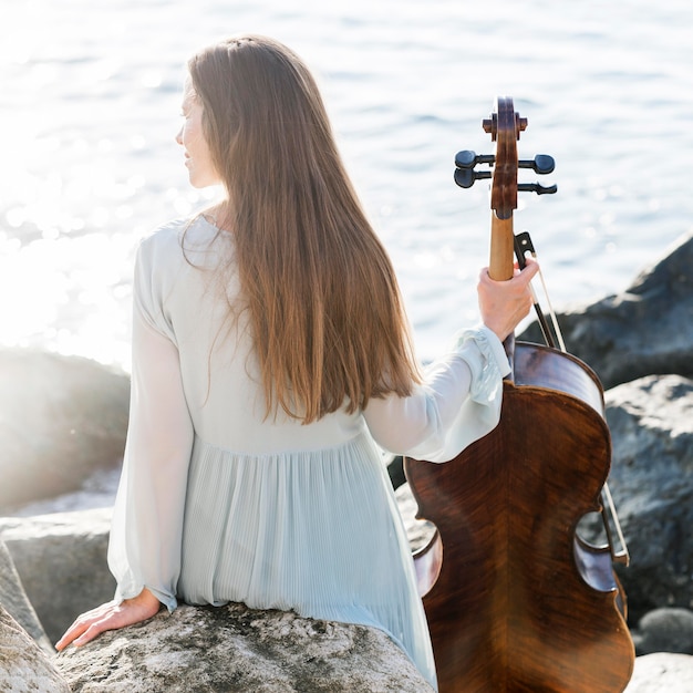 Вид сзади женщины с виолончелью на берегу моря