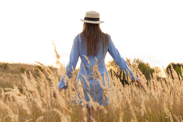 Free photo back view of woman with hat posing through the fields