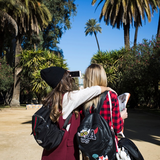 Free photo back view women with map taking selfie