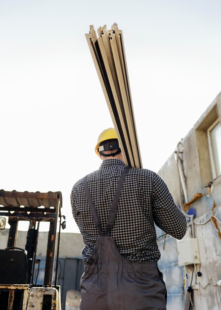 Back view of worker with hard hat carrying wood