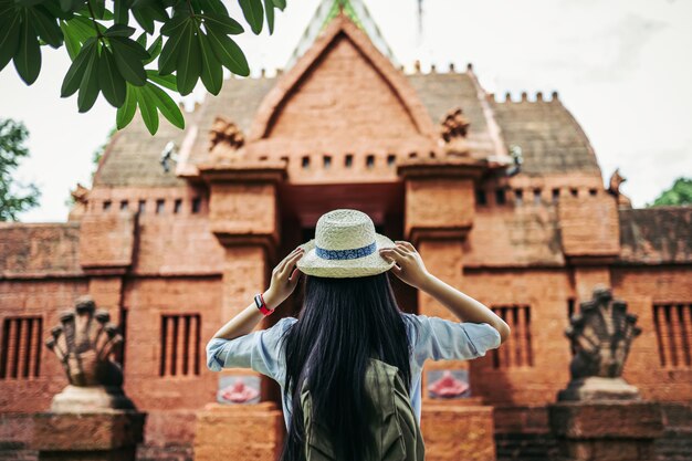 Вид сзади молодой азиатской женщины-туриста с черными длинными волосами, носящими шляпу, стоящего муравья, смотрящего на красивое древнее место или Старый храм во время путешествия в отпуске