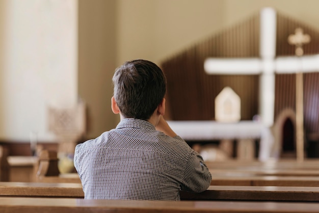 Молодой мальчик молится в церкви, вид сзади