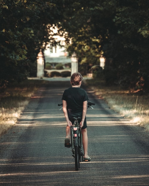 해질녘 숲길에서 손 없이 자전거를 타는 어린 소년의 뒷모습
