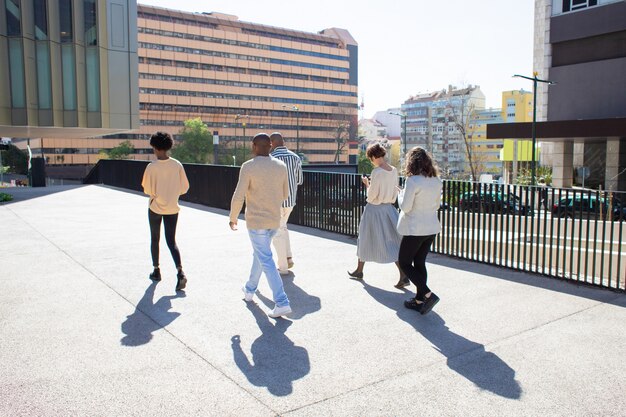 Back view of young citizens walking on street with phones