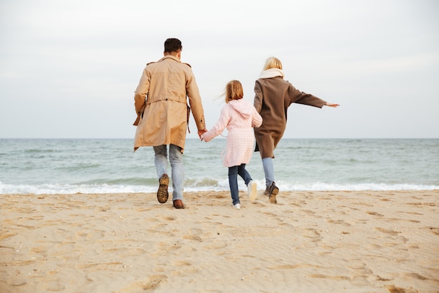 Vista posteriore di una giovane famiglia con una figlia piccola divertirsi in spiaggia insieme e in esecuzione