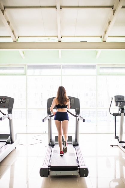 Back view of young fit woman works run on sport simulator in black sportswear and red sneakers