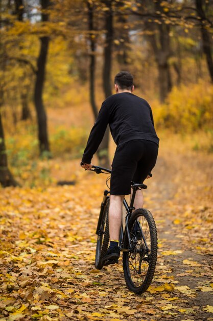 Back view of Young handsome man riding a bicycle on forest road among trees in sunset. Sports and healthy lifestyle. Trip to rainforest