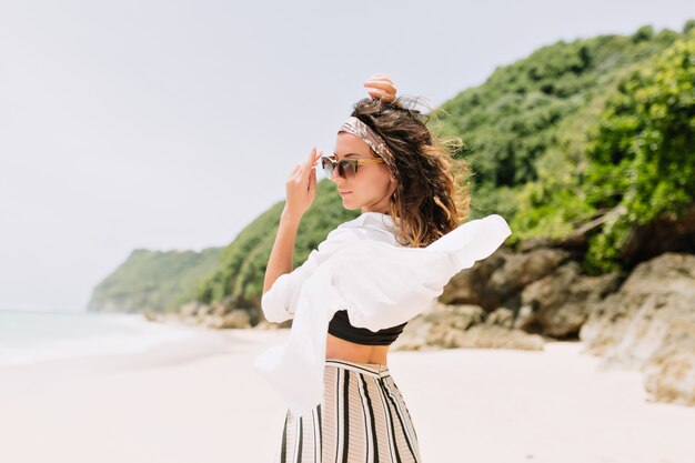 Back view of young pretty lovely woman with wavy dark hair dressed white shirt and striped pants