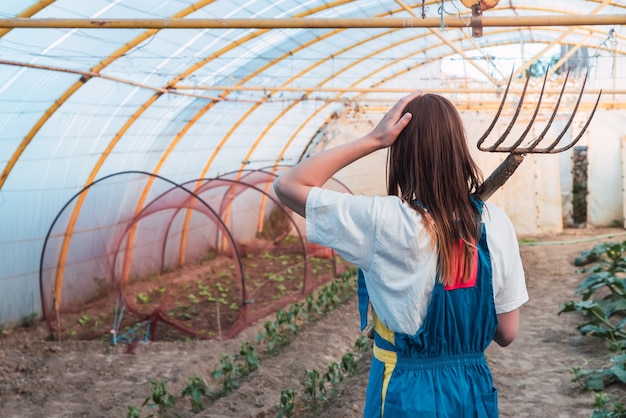 Back view of a young woman with a grass raking tool