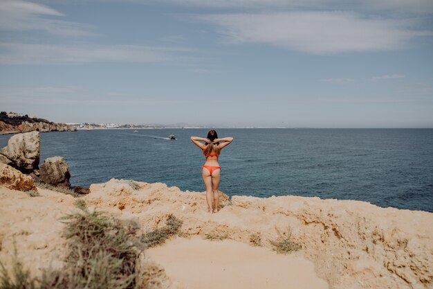 Back viewgirl in red swimsuit, with raised her arms up posing on the beach