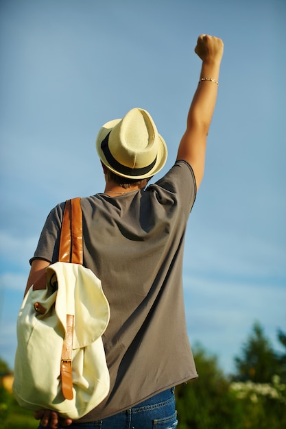 Free photo back of young attractive modern stylish man in casual cloth in hat in glasses  behind blue sky